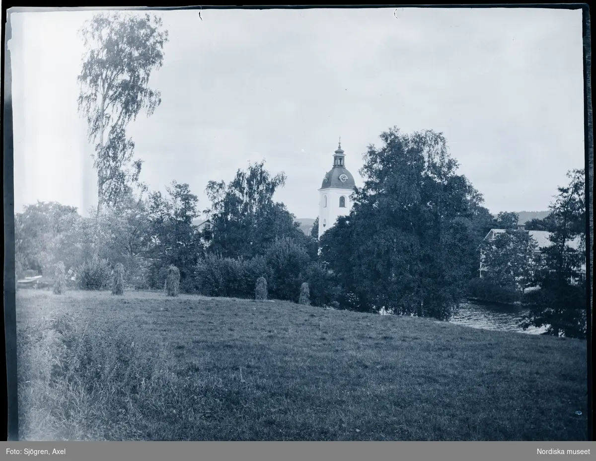 Vy över äng med hässjor, Filipstads kyrka i bakgrunden.