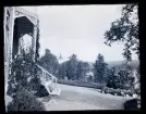 Vy över trädgård. En träbänk står placerad framför en altan med snickarglädje. I bakgrunden skymtar Filipstad kyrka.