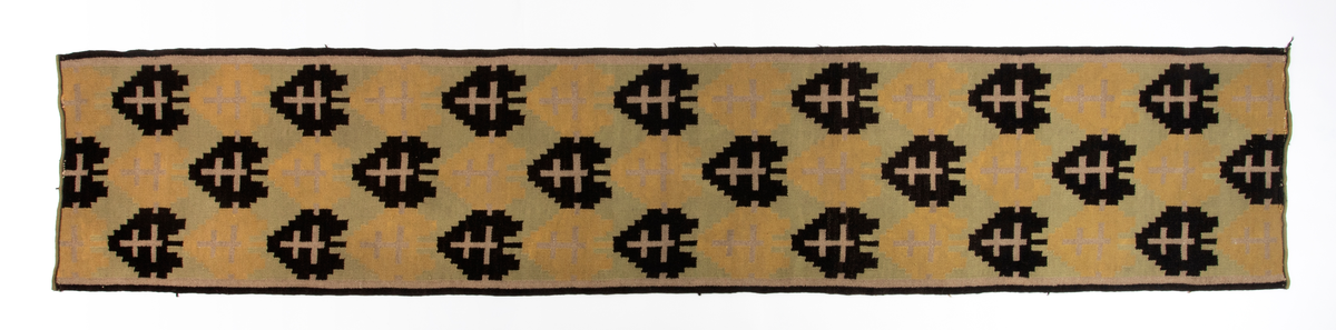 Rektangulær gulvløper i rutevevteknikk i tykt ullgarn. Innslag i svart, gult, grønt og beige på grov hamprenning. Motivet er et stilisert tre eller "hjerte" i svart og ett i gult; gjentatt regelmessig langs hele løperen.
