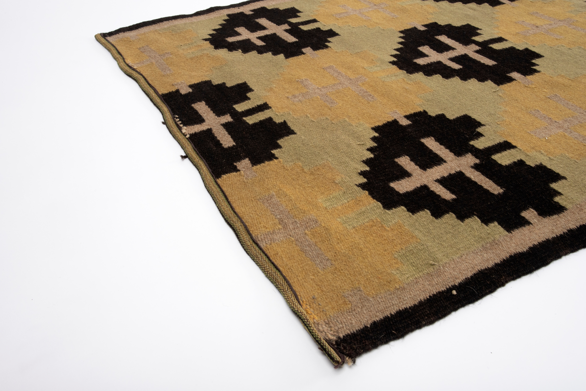 Rektangulær gulvløper i rutevevteknikk i tykt ullgarn. Innslag i svart, gult, grønt og beige på grov hamprenning. Motivet er et stilisert tre eller "hjerte" i svart og ett i gult; gjentatt regelmessig langs hele løperen.
