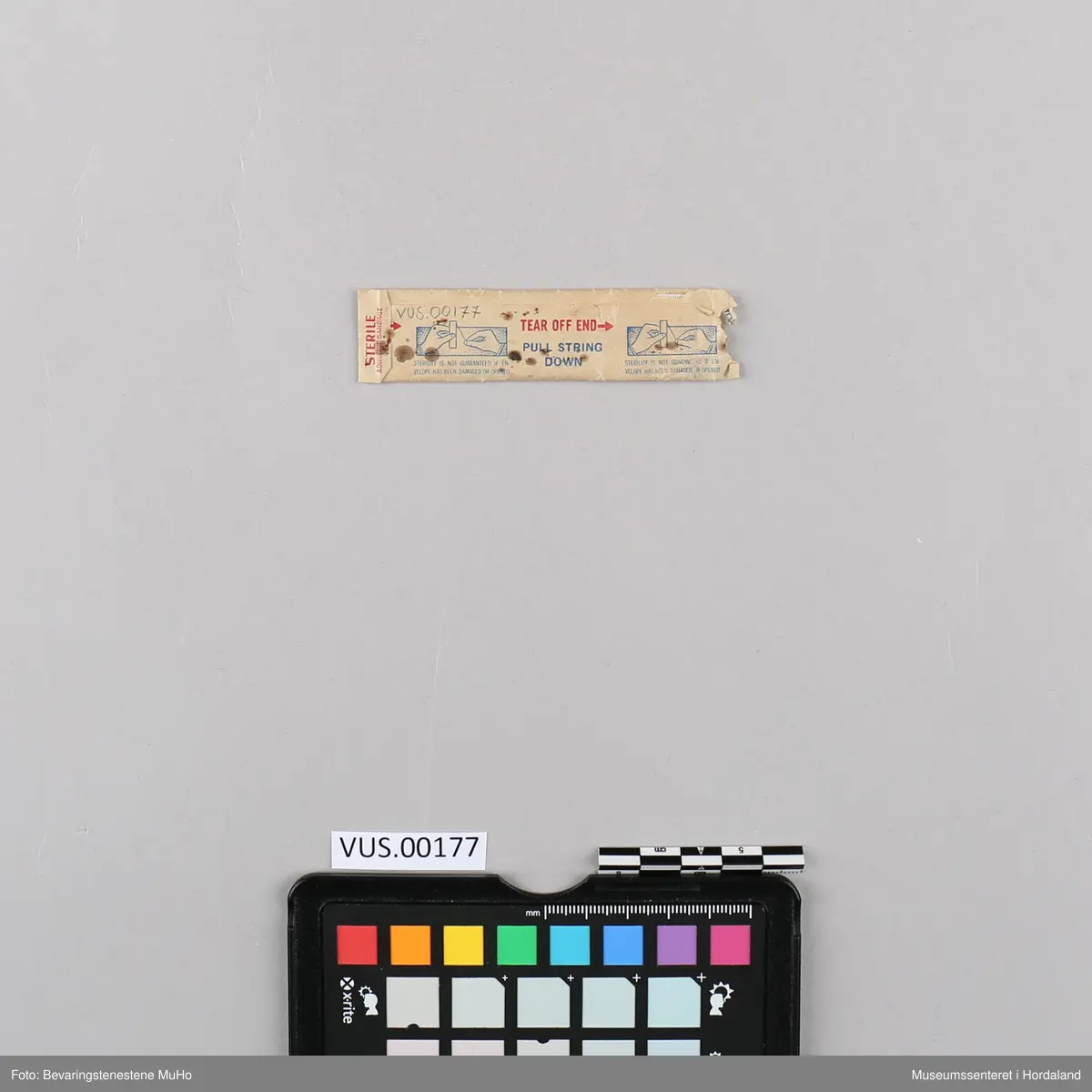 Rektangulært, hvitt plaster inni en rektangulær, beige papirlomme med bruksanvisning.