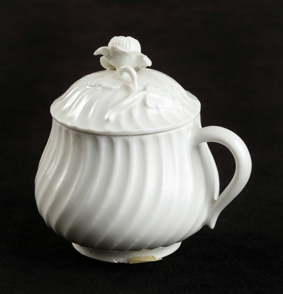 Krämkopp med lock, av porslin. Vitglaserad.
Något bukig modell, vridna räfflor å lock och knopp. På locket en skulpterad blomma som knopp.

Inskrivet i huvudbok 1967.