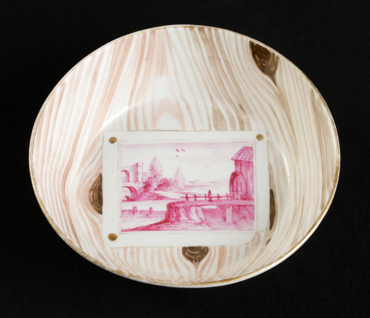 Kopp med fat av porslin. Rak bägarform med C-formad grepe. Fat med raka kanter. 
Dekorerad i träådring, med simulerade pappersblad (trompe l´oeil) och landskap i rött efter
kopparstick. Kantränder i brunt och guld.

Inskrivet i huvudkatalogen 1967.