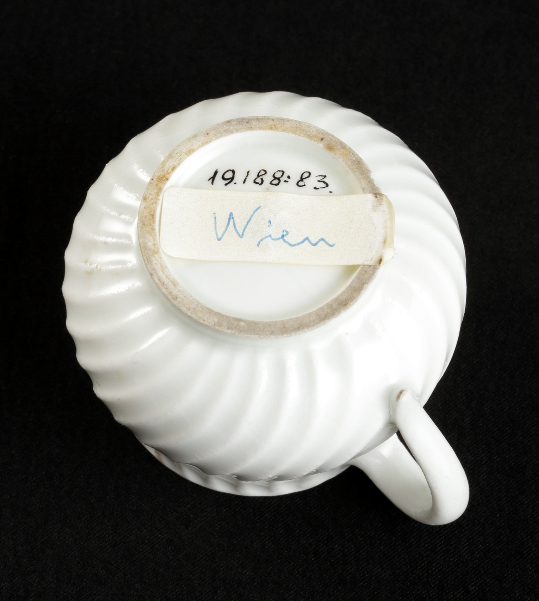 Krämkopp med lock, av porslin. Vitglaserad.
Något bukig modell, vridna räfflor å lock och knopp. På locket en skulpterad blomma som knopp.

Inskrivet i huvudbok 1967.