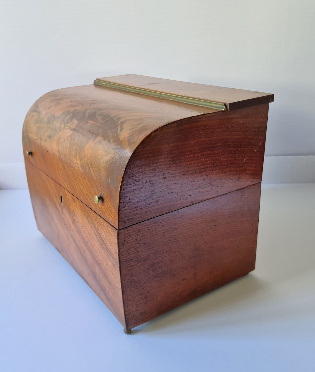 Reiseskrin med seks karafler og to glass. Skrinet er utformet i lys mahogny. Plass innvendig til seks karafler med propp, og to små stettglass. Skrinet er inndelt i seks seksjoner og trukket med mørk blå fløyel nede i rommene og (blass) rød fløyel oppe ved kantene og under lokket. I lokket er det også et spor til å feste to glass. Disse er det ikke plass til når skrinet lukkes. Hengslet lokk. Nøkkelhull foran. Nøkkel mangler.