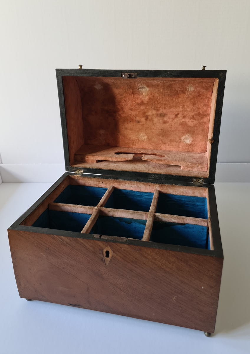 Reiseskrin med seks karafler og to glass. Skrinet er utformet i lys mahogny. Plass innvendig til seks karafler med propp, og to små stettglass. Skrinet er inndelt i seks seksjoner og trukket med mørk blå fløyel nede i rommene og (blass) rød fløyel oppe ved kantene og under lokket. I lokket er det også et spor til å feste to glass. Disse er det ikke plass til når skrinet lukkes. Hengslet lokk. Nøkkelhull foran. Nøkkel mangler.