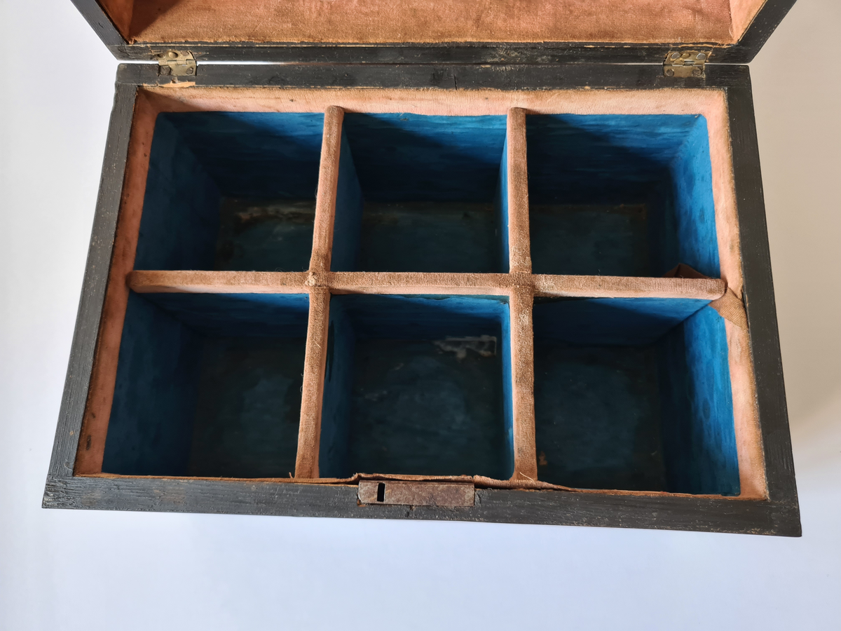 Reiseskrin med seks karafler og to glass. Skrinet er utformet i lys mahogny. Plass innvendig til seks karafler med propp, og to små stettglass. Skrinet er inndelt i seks seksjoner og trukket med mørk blå fløyel nede i rommene og (blass) rød fløyel oppe ved kantene og under lokket. I lokket er det også et spor til å feste to glass. Disse er det ikke plass til når skrinet lukkes. Hengslet lokk. Nøkkelhull foran. Nøkkel mangler.