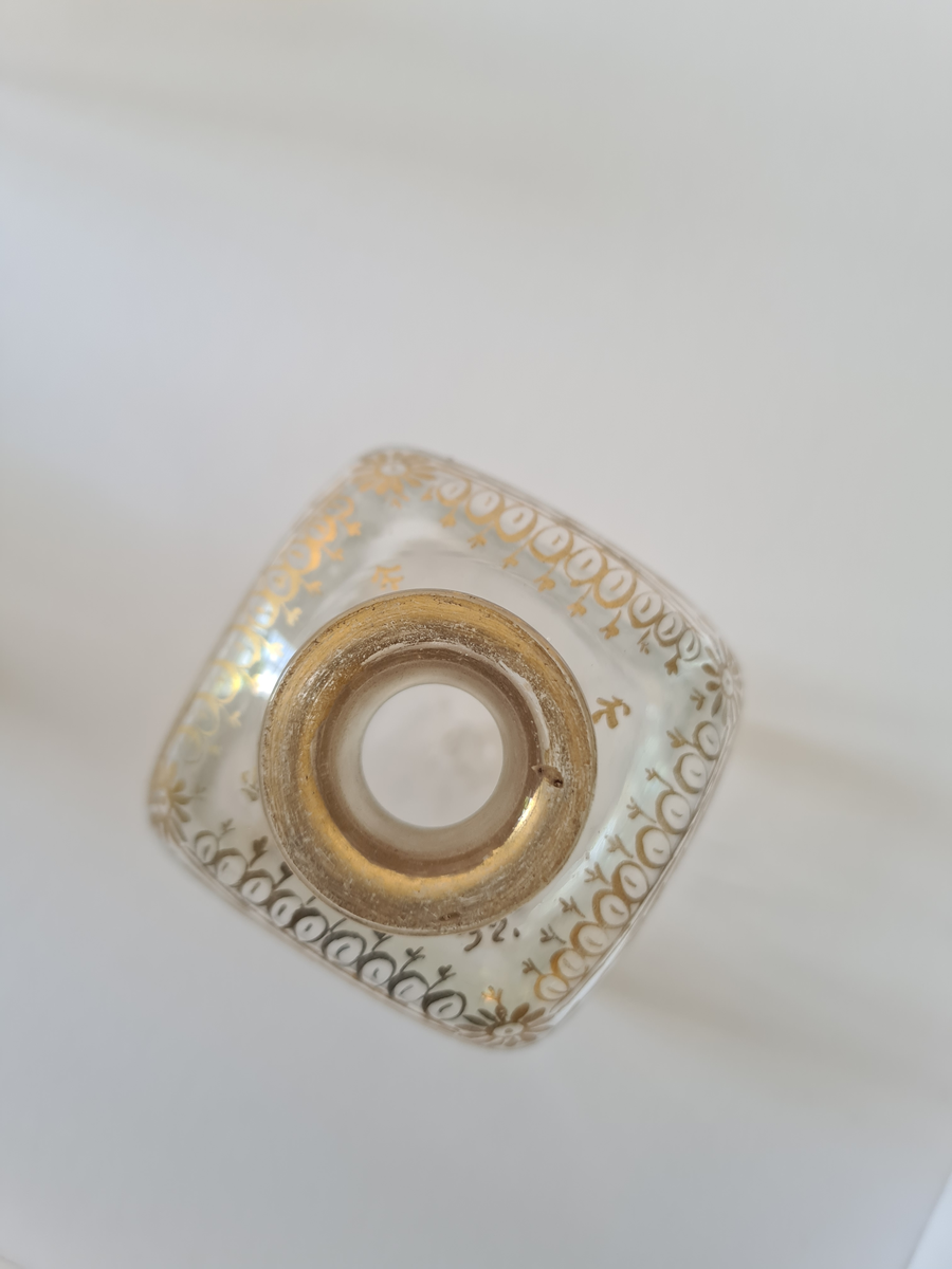 Karaffel av glass med tilhørende propp. Forgyllet dekor rundt halsen. Firkantet form, noe avrundet ved halsen.