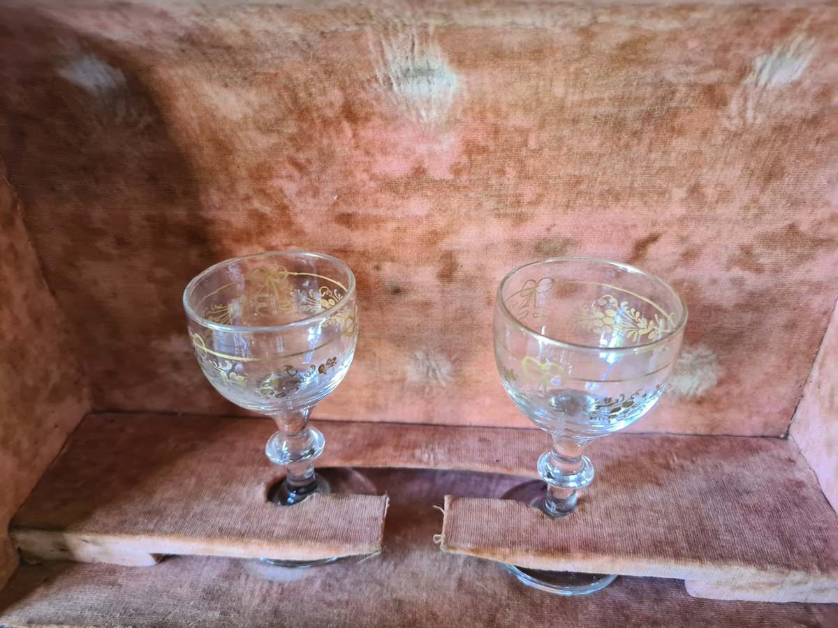 Reiseskrin med seks karafler og to glass. Skrinet er utformet i lys mahogny. Plass innvendig til seks karafler med propp, og to små stettglass. Skrinet er inndelt i seks seksjoner og trukket med mørk blå fløyel nede i rommene og (blass) rød fløyel oppe ved kantene og under lokket. I lokket er det også et spor til å feste to glass. Disse er det ikke plass til når skrinet lukkes. Hengslet lokk. Nøkkelhull foran. Nøkkel mangler.