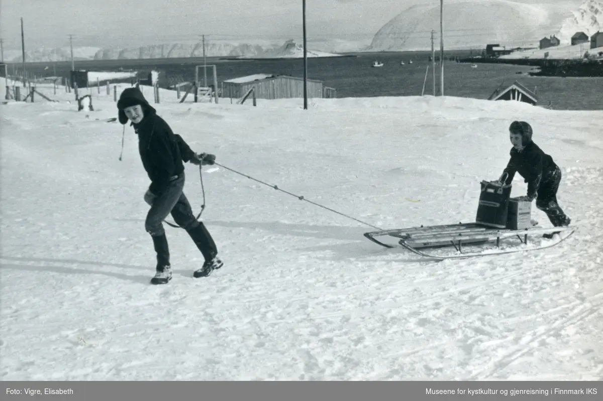 Sarnes. To gutter fra Solvang internatet med en slede med bagasje/varer. Deler av bebyggelsen i bakgrunnen. 1960/61.