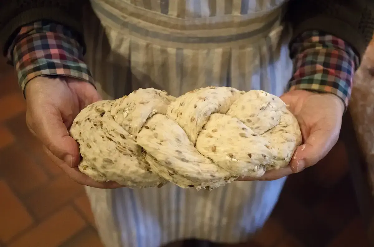 En kinne holder et flettet brød som er klart til å settes inn i ovnen.