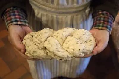 En kinne holder et flettet brød som er klart til å settes inn i ovnen.