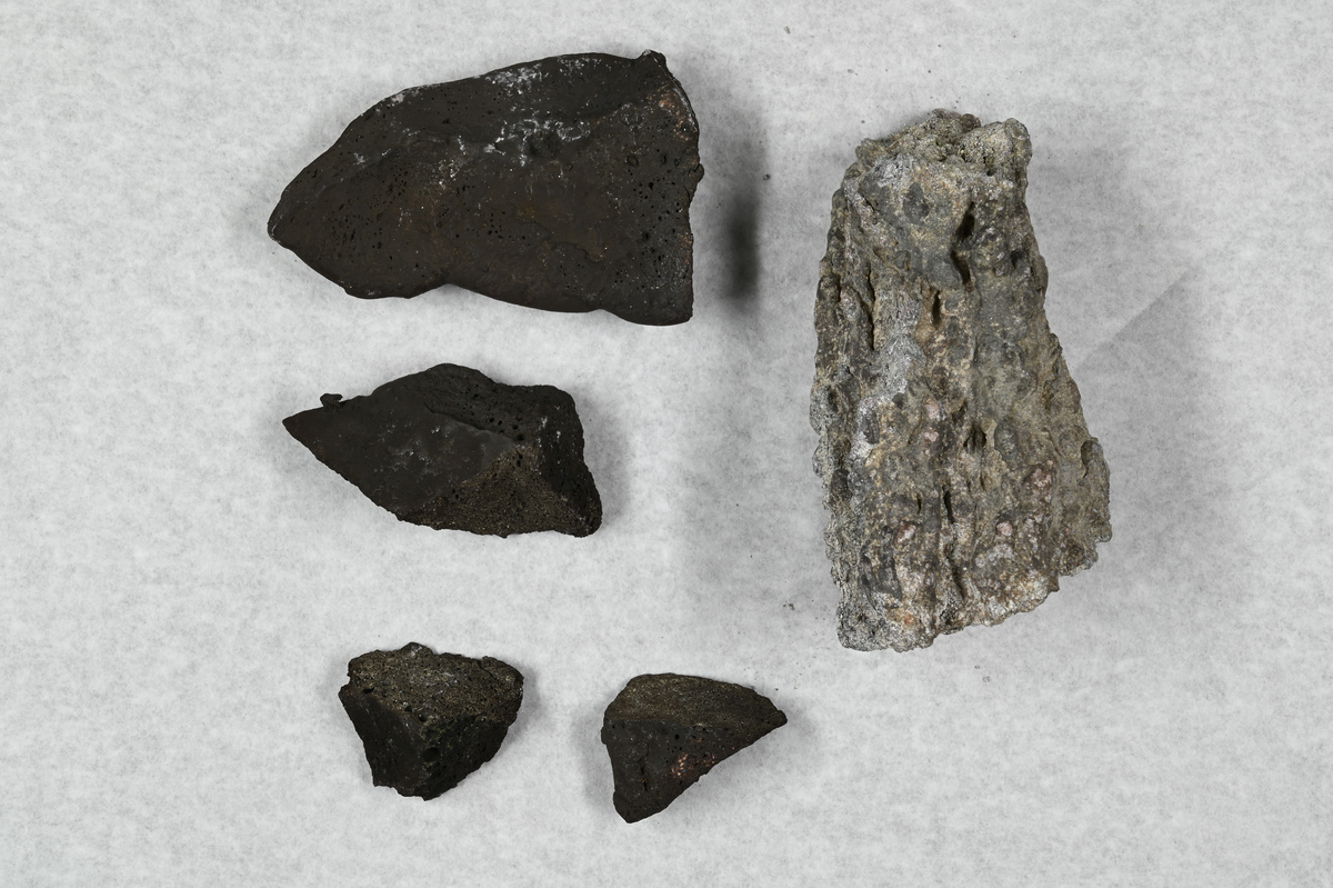 Fem materialprover, fyra svarta och ett vit och gråaktigt. Tillhörande lapp med notering: "Speiss, erhållen i Garhärd, Sågmyra 1869".