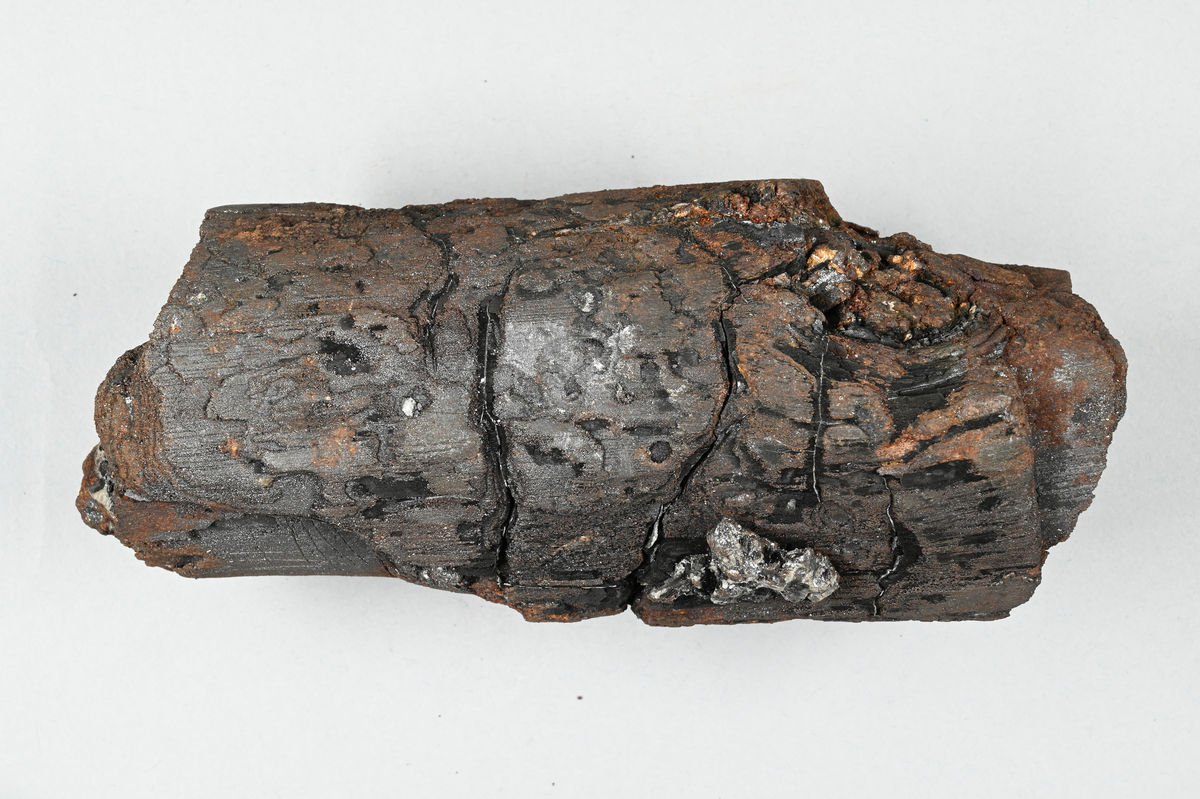 Prov av träkol som genomgått metamorfos, svart och brunaktig. Provet har ett tillhörande brev med kuvert. Brevet var adresserat från: "Morgårdshammars Mek. Verkstads Aktiebolag, Morgårdshammar". Brevet noterade: "Morgårdshammars Mek. Verkstads Aktiebolag. Morgårdshammar den 25/10 1928. Herr Professor Arvid Johansson, Bergshögskolan, STOCKHOLM. Broder. Tager mig härmed friheten tillsända Dig en låda, innehål-lande 1 st. träkol, som undergått en i mitt tycke underlig metarmor-fos och har jag visat den för en del hytteknici, som förklarat den rent unik. Det var efter nedblåsningen av Köpings Hytta 1918, som kolet fanns sittande i murväggen under formnivån enligt utsago av den arbetare, som påträffade det. Om du nu anser den av något värde kan den ju lämpligen införlivas med Bergshögskolans samlingar eller eventuellt där Du kan anse den passa. Samtidigt sänder jag ett sigill från Ing. Anckert, Smedjebacken, som han för sin del ansåg borde hemmahöra bland Tek-niska Museets samlingar, men förmodar jag att han ej har något e-mot om Bergshögskolan tager hand därom, ifall Du anser lämpligt så. Hälsningar från Din tillgivne, Filip Södermans (?)."