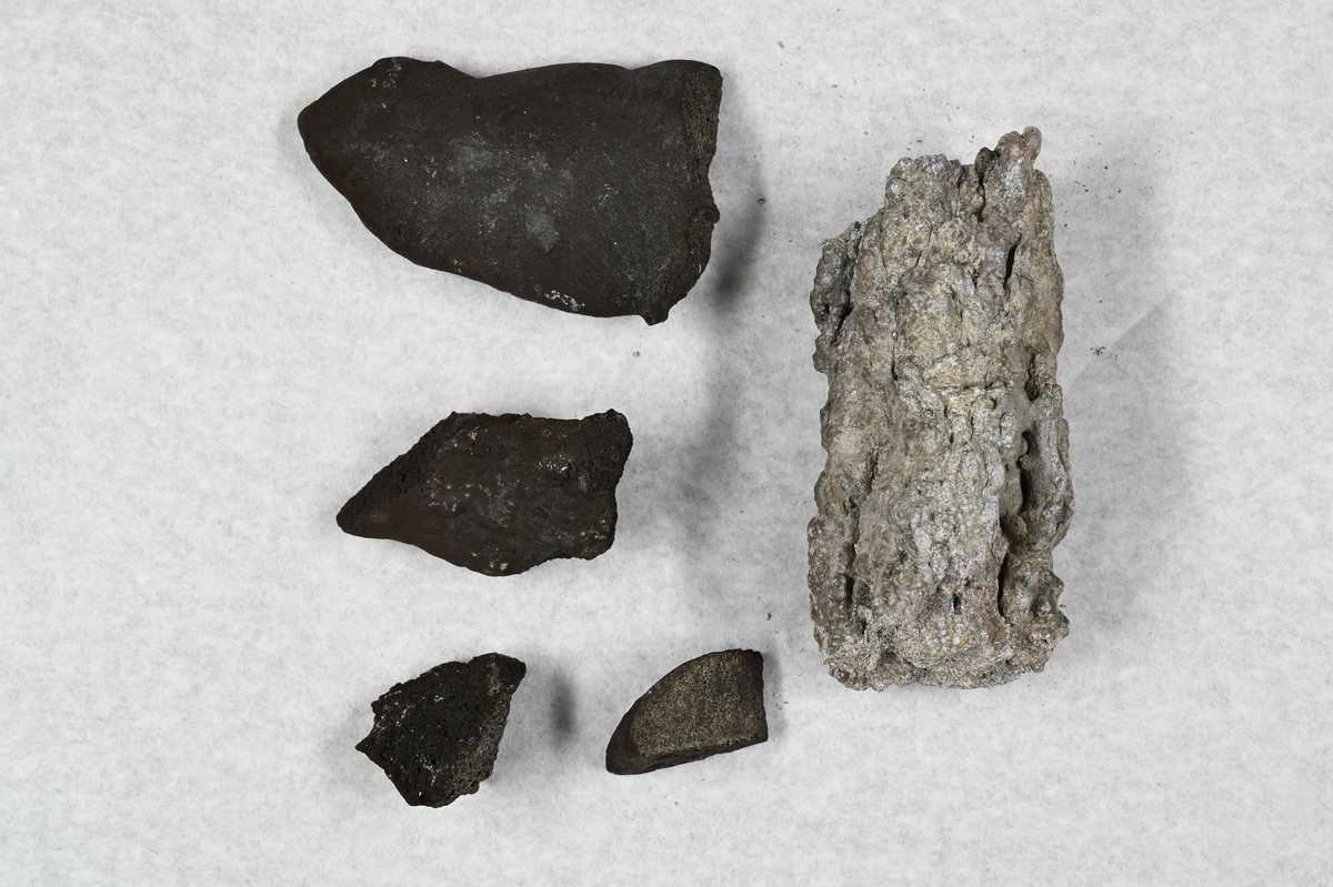 Fem materialprover, fyra svarta och ett vit och gråaktigt. Tillhörande lapp med notering: "Speiss, erhållen i Garhärd, Sågmyra 1869".
