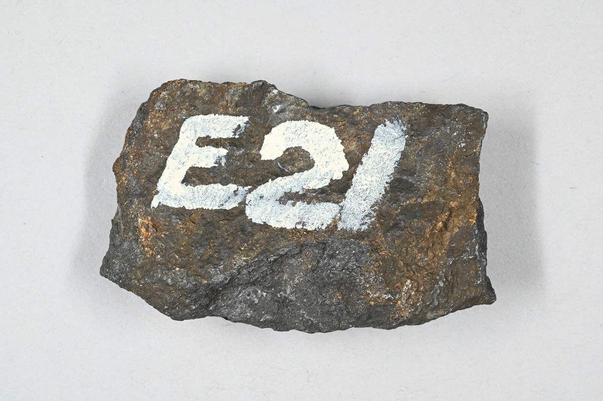 Prov av grafit, grå och brunaktig. Märkning på provet i vit färg: "E21. Norbergs-grafit. O-A."