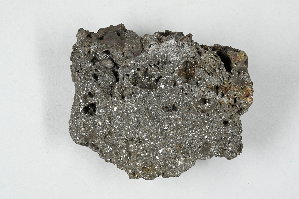 Slaggprov, grå och rödaktig med metalliskt skimmer. Tre tillhörande lappar. Två av lapparna noterar: "Garpenberg, Sulu slagg". En noterar: "Rydén".