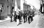 Kortege med fanbärare och musikkår framför unga och gamla på Brahegatan i Gränna.