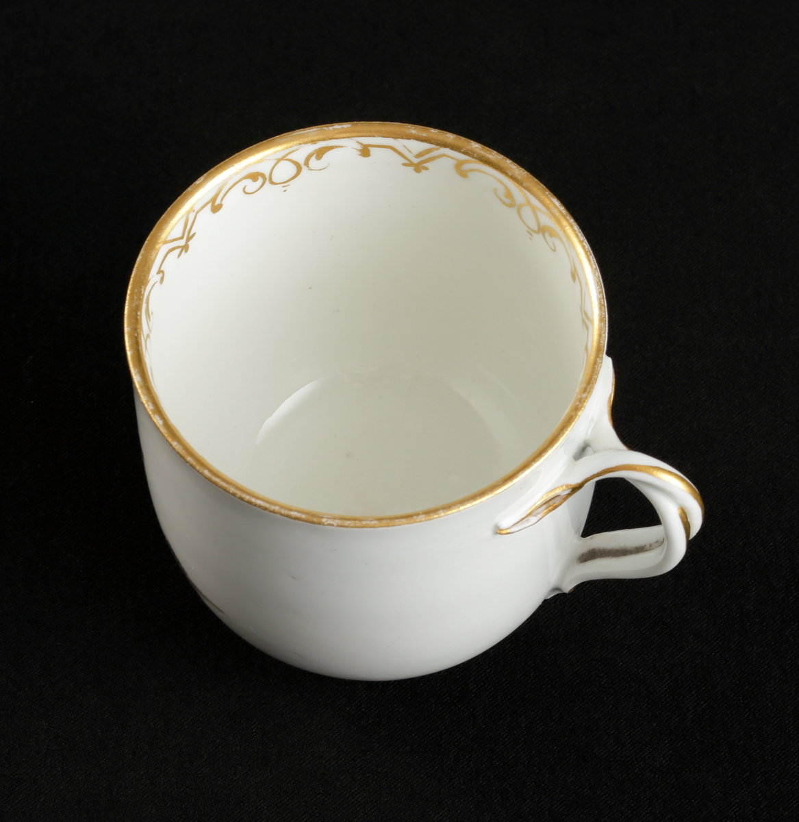 Kopp med fat av porslin. Koppen i bägarform. Fatet skålformigt. 
Dekorerad med ruinlandskap i svart camaïeu, med färglagda figurer. 
Kring kanterna spetsliknande bårder i guld. 

Inskrivet i huvudbok 1967.