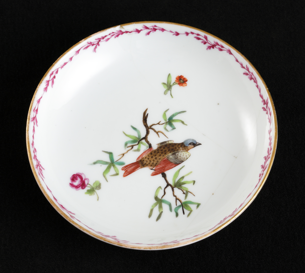 Kopp med fat, av porslin. Skålformad. 
Dekorerad med fågel på trädgren och strödda blommor. Längs kanterna lagergirland i rosa och guld.

Inskrivet i huvudbok 1967.