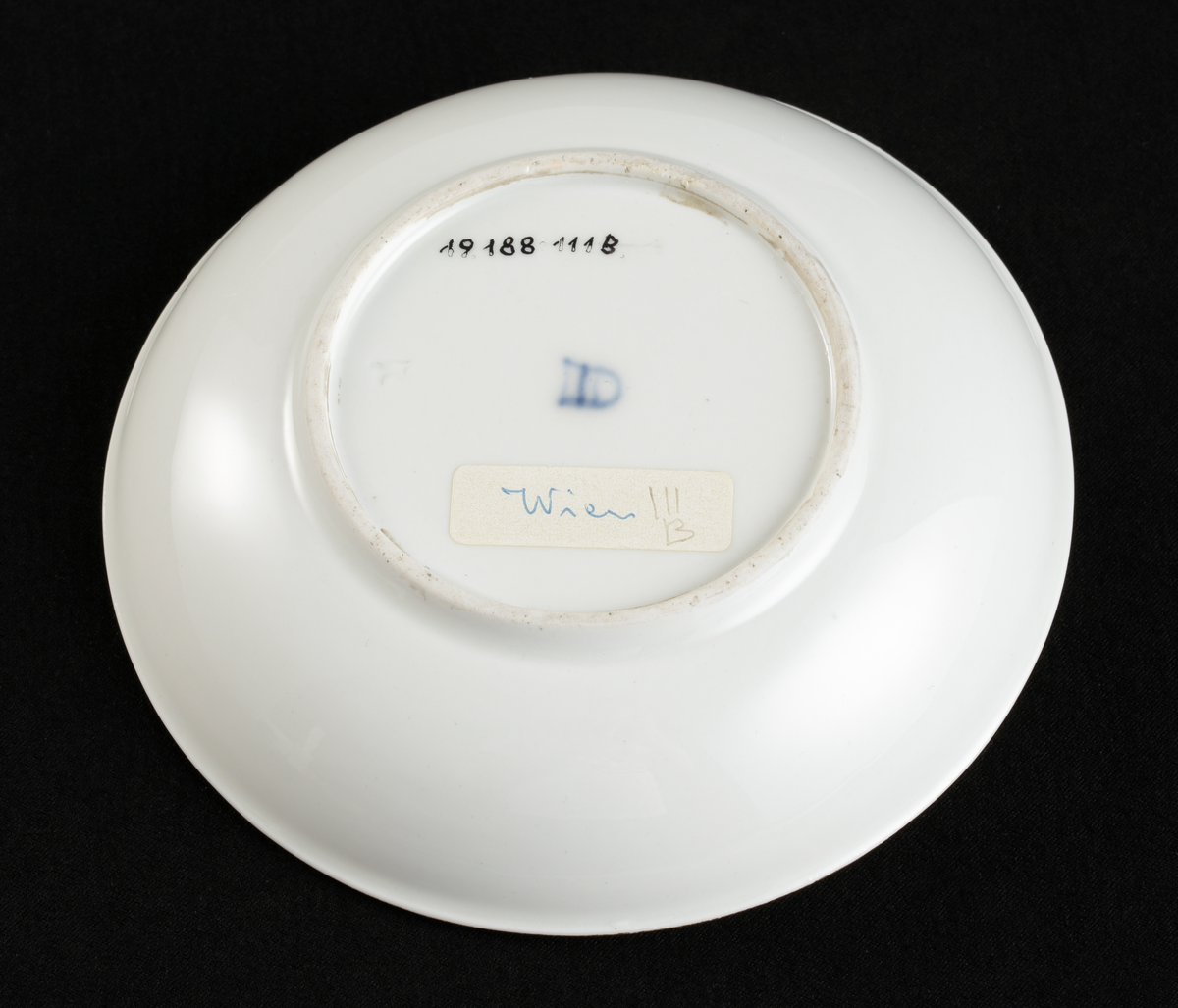 Kopp med fat av porslin. Koppen i bägarform. Fatet skålformigt. 
Dekorerad med ruinlandskap i svart camaïeu, med färglagda figurer. 
Kring kanterna spetsliknande bårder i guld. 

Inskrivet i huvudbok 1967.