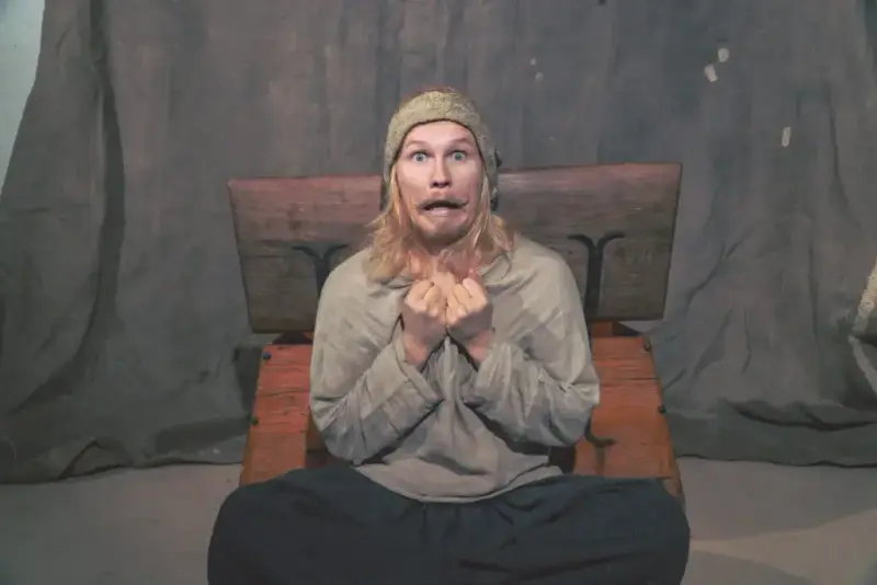 Ung mann i middelaldersk naturfarget linskjorte og hatt som ser forskrekket ut