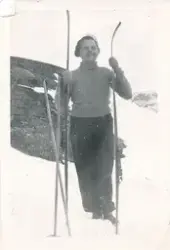 En kvinne står i snøen med ski og skistaver i hendene. Hun s