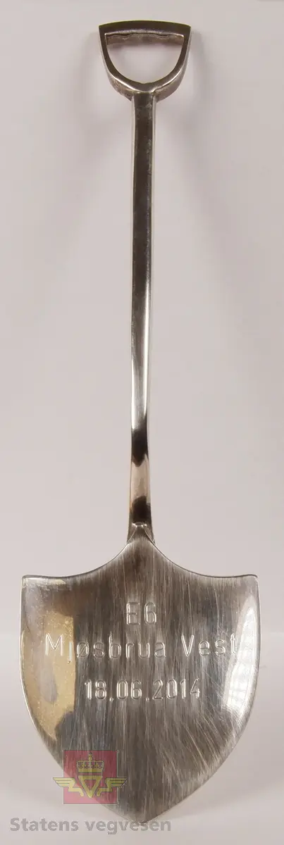 Sølvskje formet som en liten spade med håndtak, beskyttet i et hvitt etui. 