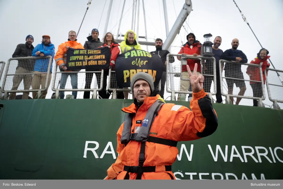 Skådespelaren Gustaf Skarsgård står framför båten Rainbow Warrior III.
I bakgrunden står delar av besättningen på Rainbow Warrior.