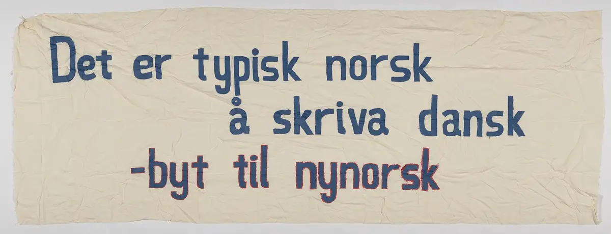 Banner frå arkivet til Norsk Målungdom. På banneret står teksten: "Det er typisk norsk å skriva dansk - byt til nynorsk". Det er truleg at banneret har vore i bruk under ein aksjon for Norsk Målungdom.
