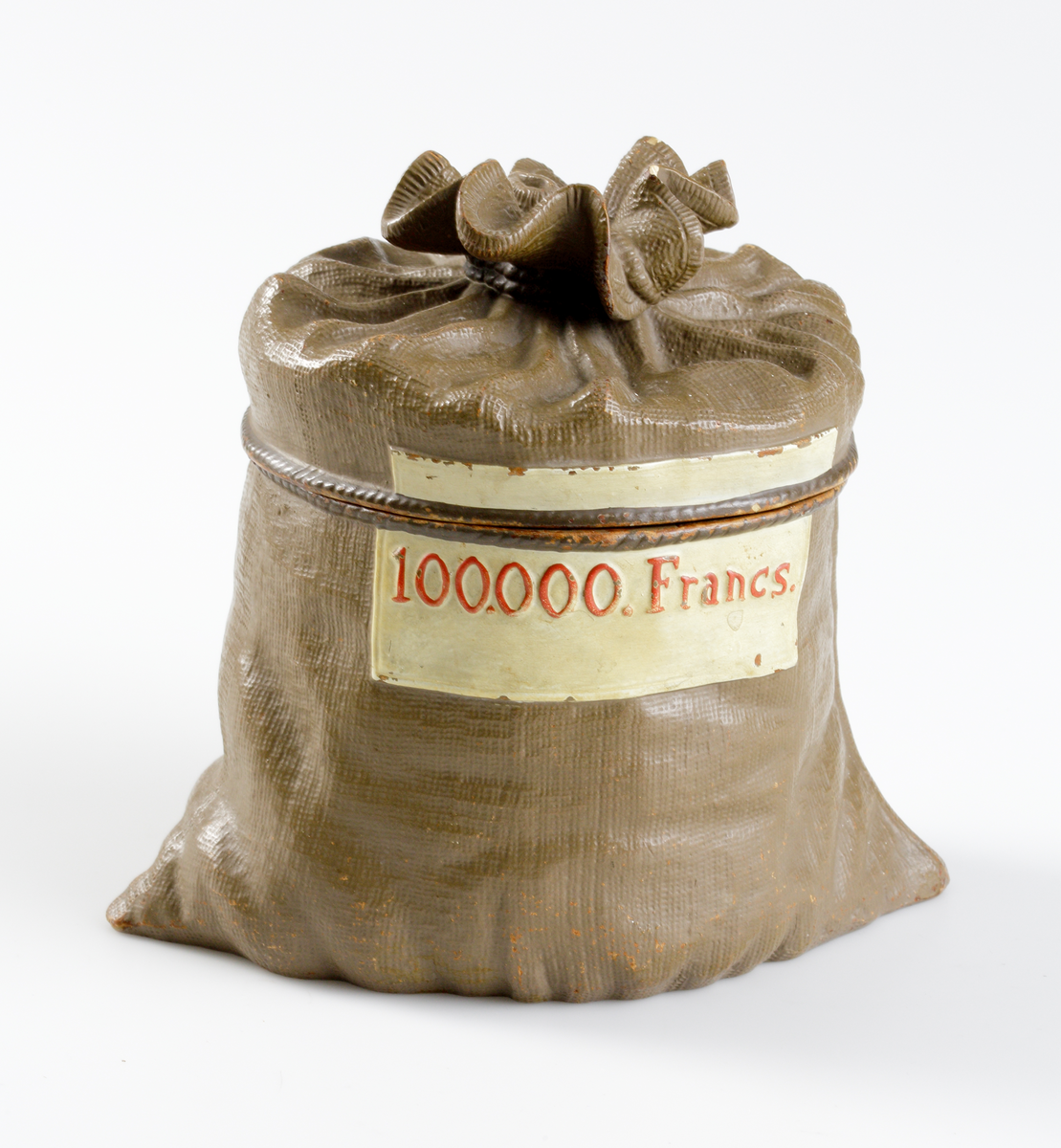 Tobaksburk av lergods, i form av gråbrun naturtrogen pengasäck. Runt locket ett "snöre" med rött sigill.
Märkt på livet med vit etikett: "100.000 Francs".

Inskrivet i huvudbok 1947.