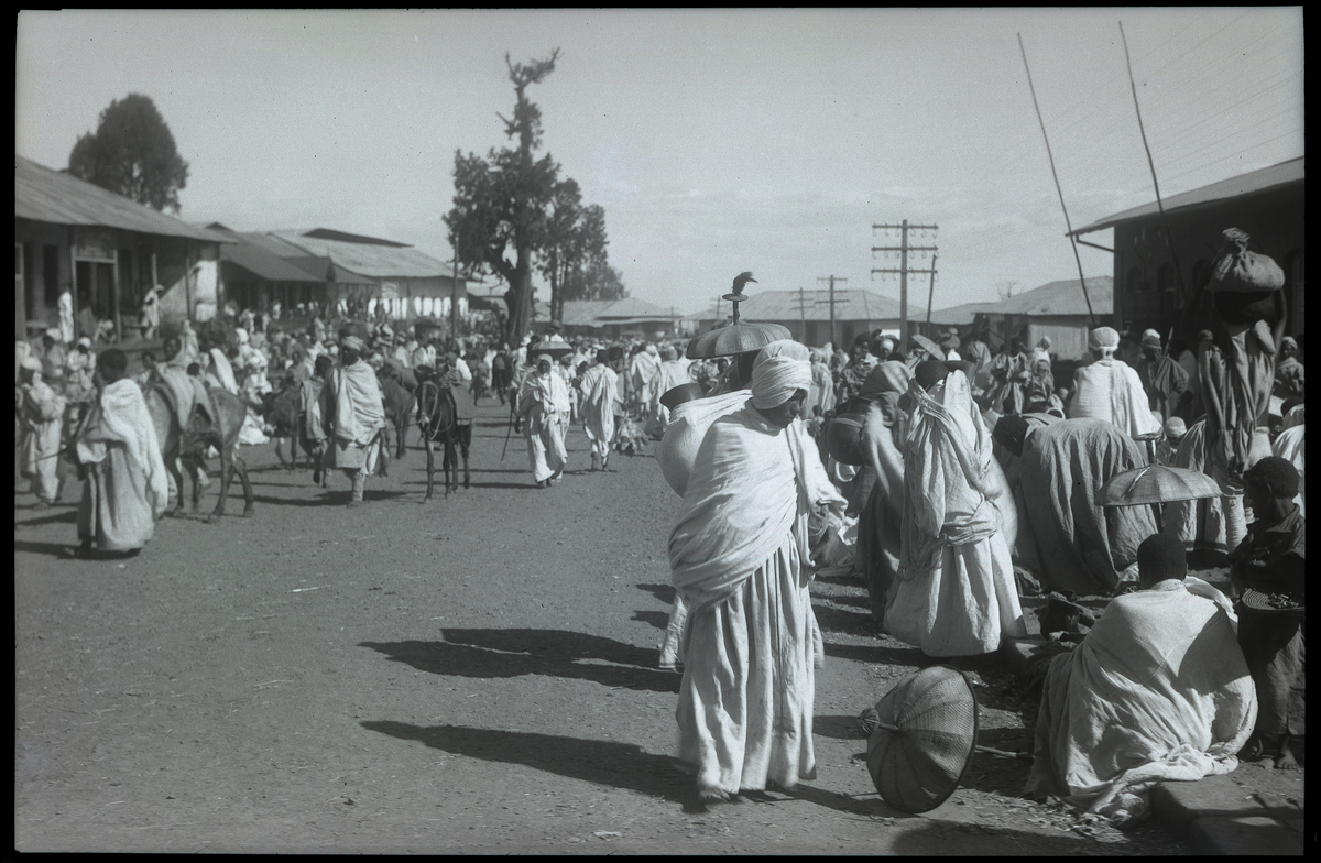 Foto tatt under reise i Afrika. Folkemengde rundt marked i Addis Ababa, hovedstaden i Etiopia 

I folkemengden kan man se etiopiske parasoller 

Påskrift på konvolutt negativ lå i: Adis Ababa