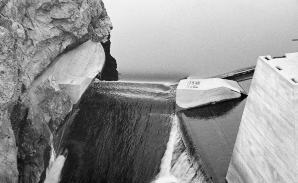 Dette fotografiet viser antakelig Sølvstudammen i Ågårdselva – Glommas vestre løp i daværende Tune kommune i Østfold – fotografert etter at den nye Sølvstudammen var ferdig, antakelig i slutten av 1930-åra. Fotografiet viser en dam, støpt av armert betong, med en åpning, et «løp» for vannet mot en steil bergvegg på den ene elvebredden. Bildet er tatt i motstrøms retning.

Ågårdselva er et cirka fem og en halv kilometer langt vassdrag som renner fra den nordvestre enden av Isnesfjorden (Vestvannet) i Nedre Glommas vestre løp, sørvestover gjennem berglendt terreng mot innsjøen Visterflo. Høydeforskjellen mellom Isnesfjorden og Visterflo er på bortimot 25 meter. Ågårdselva har tre fossefall, det øverste her ved Sølvstu, deretter ved Valbrekke og nederst ved Solli. Behovet for den dambygginga vi ser på dette fotografiet var forårsaket av selskapene Borregaards og Hafslunds inngrep i Glommas østre løp, hovedløpet, som i lavvannsperioder gjorde det svært vanskelig å få tømmer som skulle til bedrifter nedenfor Sarpsfossen via Mingevannet, Isnesfjorden og tømmertunnelen til Eidet gjennom det trange sundet ved Trøsken. Dette forsøkte man å løse ved å heve vannspeilet i Isnesfjorden med en dam som skulle plasseres 10-15 meter ovenfor den eksisterende dammen ved Sølvstufossen. Se mer informasjon under fanen «Opplysninger».