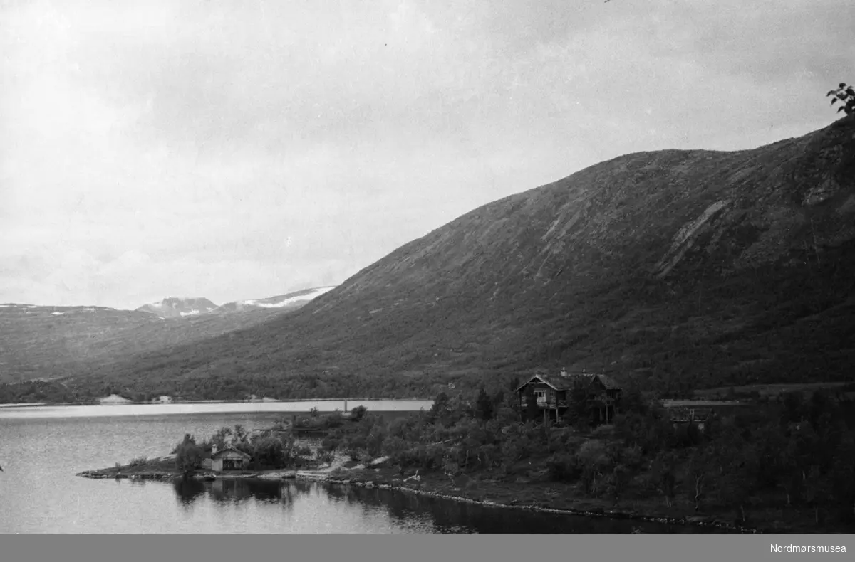 Foto av en eldre fjellgård omgitt av fjord og fjell. Det er ukjent hvor og når bildet er fotografert. Fra arkivet etter John Myren.