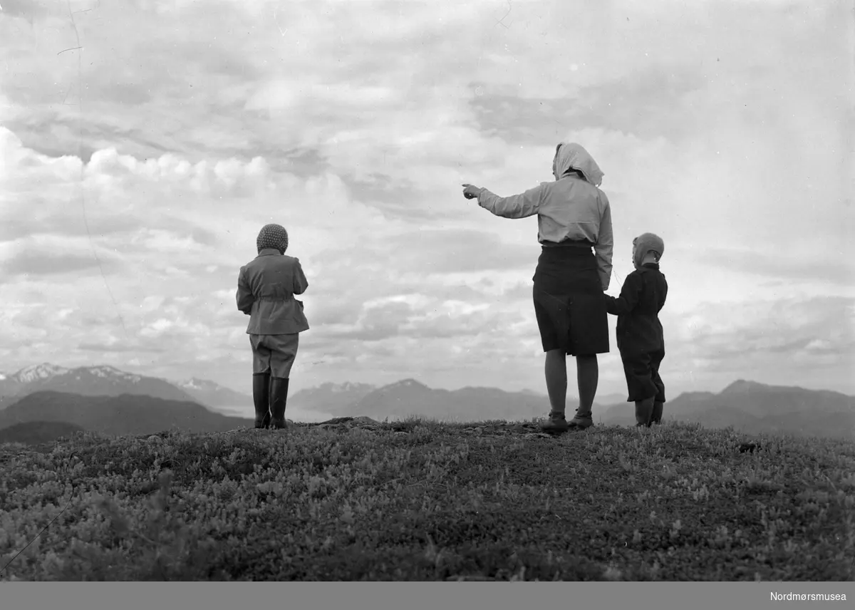 En kvinne med to barn speider utover mot fjellene. Det er ukjent hvem vi ser på bildet, samt hvor og når bildet er fotografert. Fra arkivet etter John Myren.