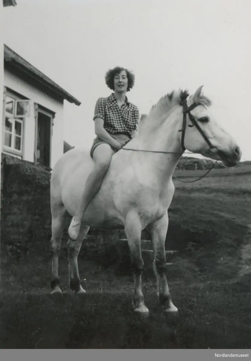 Ung kvinne som sitter på en hest. Anna Dortea Kristensen (f. 1935) sitter på hesten Truls på gården Mjelde på Engeløya i Steigen.