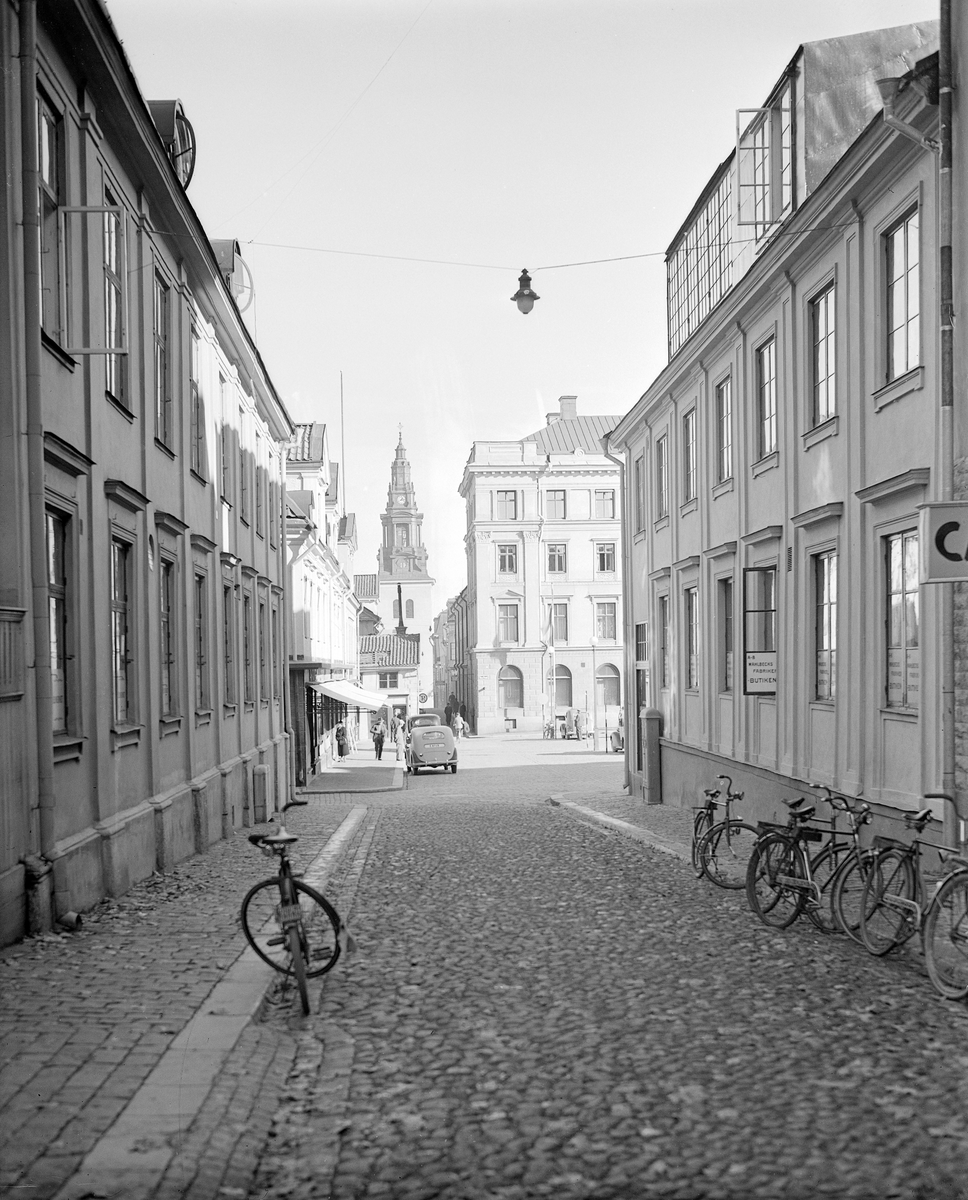 Parti av Domkyrkogatan i Linköping. I blickfånget Stora torgets norra del med en skymt av Stora hotellet. I fonden Sankt Larskyrkan. I bildens sammanhang stannar vi gärna upp vid det stora fönsterpartiet i vindsvåningen till höger. Med sitt tilltagna ljusinsläpp från norr skvallrar partiet om en fotoateljé. Möjligtvis tillkom ateljén när konstnären och fotografen Didrik von Essen skrev sig på adressen 1895. Från 1905 till sin död 1912 drevs ateljén av Tekla Engström, som tidigare haft sin fotofirma inkvarterad i Lagerströmska gården vid Stora togets nordöstra hörn. Efter Engström övertogs ateljén 1913 av Regina Andersson, bördig från Örebro men inflyttad från Stockholm. Omkring 1930 avvecklade hon sin verksamhet och därefter talar källorna tyst om någon fortsatt fotorörelse på adressen. Odaterat fotografi som antas tillkommet vid 1930-talets sista hälft.