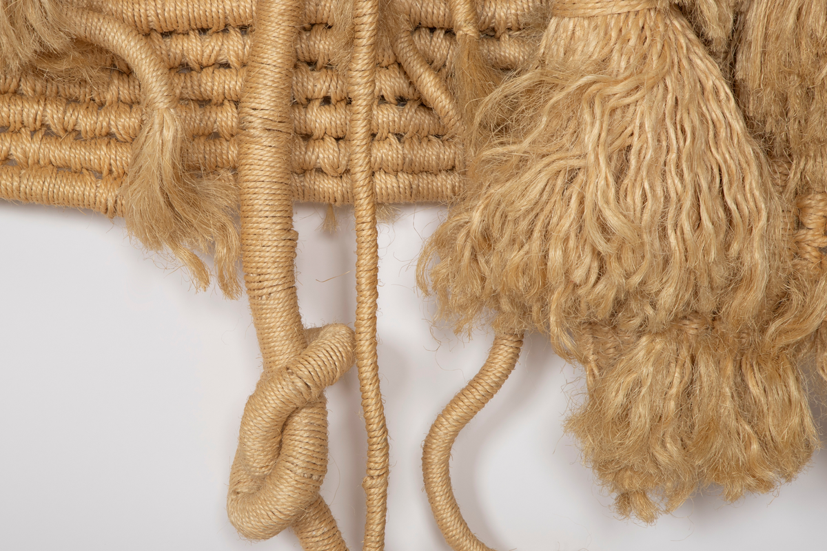 Billedvev av naturfarget sisal. Bunter av omviklede renningstråder er delvis sammenvevd til flater, delvis festet til flaten som lange pølser og løsthengende haler. Tekstilet er vevd i tre deler med et rektangulært midtfelt mellom to tilnærmet rektangulære sidefelt. Sidefeltene er glatte, mens midtfeltet fremstår frodig med lange og korte nedhengende duskehaler, de lengste så lange at de kryper ned fra veggen og utover gulvet.