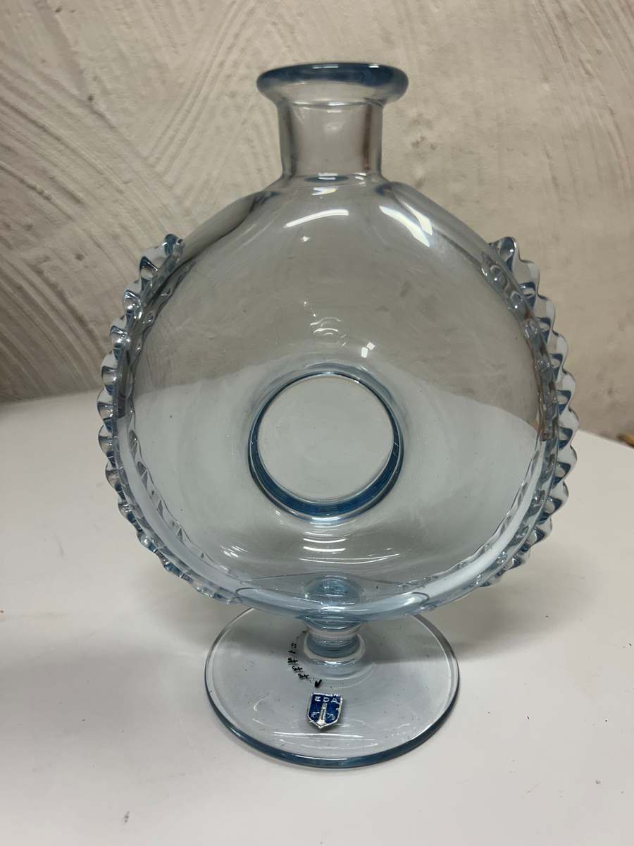 Karaff med propp, av blåtonat glas. Rund fot, flat form, intryckt på mitten, kort hals med utvikt mynningskant, strålformad dekor på ytterkanter och propp.