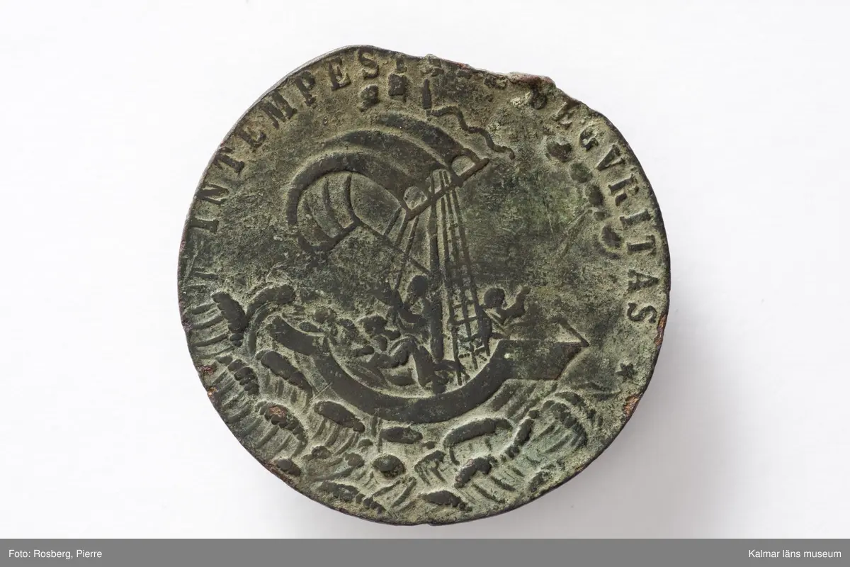 KLM 44234. Medaljong, skyddsmedaljong. Av brons. Sankt Göran-medaljong. Vikt 17,87 g. Avbrutet hänge. Åtsidan, motiv: S:t Göran och draken, text: S:GEORGIVS EQVITVM PATRONVS (S:t Georg, ryttarnas skyddspatron). Frånsidan, motiv: Kristus och hans lärjungar ombord på ett segelfartyg under storm, text: IN TEMPESTATE SECVRITAS (säkerhet i stormen).