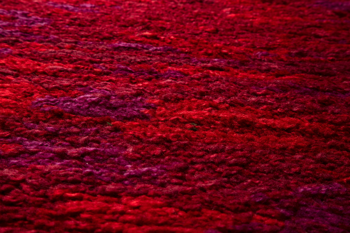 Stort gulvteppe/rye i ull i ulike rødnyanser og fiolett. Vevd teppe med floss på oversiden.