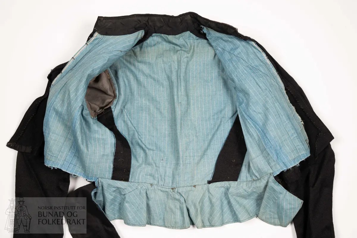 Kjoleliv av svart, kypertvevd ull. 
Kanta med svarte ullbånd med innvevd svart mønster. 
Foret er av bomullslerret med blå bunn, og smale hvite striper.
Midt foran lukkes dette stoffet som en bluse, med hekter. Øverst er det påsydd en skrå kant av det svarte stoffet, dette lukkes med trykknapper.
Livet har høy hals, kanta med bånd, denne lukkes med hekter. Over dette legges nok et lag med det svarte ullstoffet, dette lukkes midt foran med en trykknapp. Og gir en v-ringing som gjør halsen og deler av det svarte stoffet under synlig. 
Livet har et legg på hver skulder, som er med på å gi volum til brystpartiet.
Tosømsermer med litt puff, kanta nederst med bånd.
Nederst er det festa en kappe av svart bomullssateng, denne samler vidden i livet.
Midt bak er det festa tre hekter øverst på denne kappa. 
Kappa er delvis spretta av, den henger ikke lenger på livet foran. 
Nederst på ermene er livet fora med den samme svarte bomullsatengen som kappen er sydd av.
Maskinsydd med noen håndsydde detaljer.