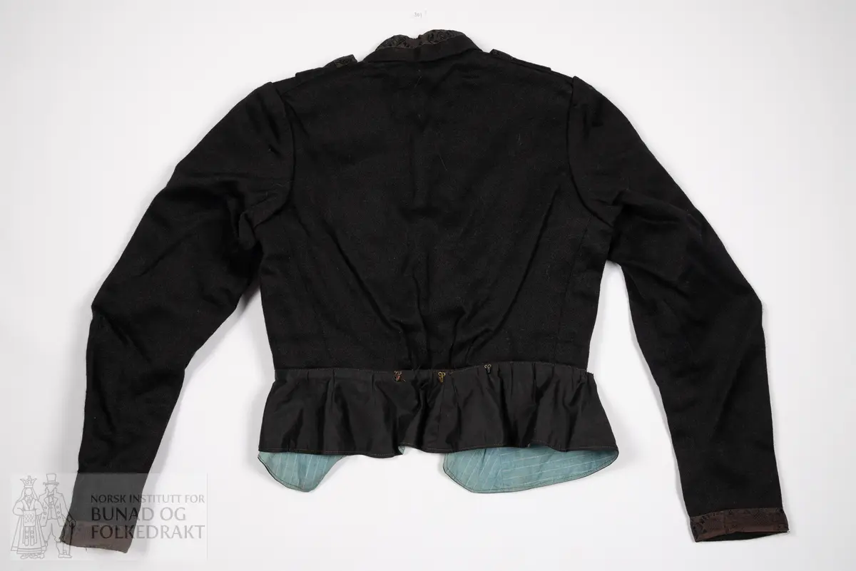 Kjoleliv av svart, kypertvevd ull. 
Kanta med svarte ullbånd med innvevd svart mønster. 
Foret er av bomullslerret med blå bunn, og smale hvite striper.
Midt foran lukkes dette stoffet som en bluse, med hekter. Øverst er det påsydd en skrå kant av det svarte stoffet, dette lukkes med trykknapper.
Livet har høy hals, kanta med bånd, denne lukkes med hekter. Over dette legges nok et lag med det svarte ullstoffet, dette lukkes midt foran med en trykknapp. Og gir en v-ringing som gjør halsen og deler av det svarte stoffet under synlig. 
Livet har et legg på hver skulder, som er med på å gi volum til brystpartiet.
Tosømsermer med litt puff, kanta nederst med bånd.
Nederst er det festa en kappe av svart bomullssateng, denne samler vidden i livet.
Midt bak er det festa tre hekter øverst på denne kappa. 
Kappa er delvis spretta av, den henger ikke lenger på livet foran. 
Nederst på ermene er livet fora med den samme svarte bomullsatengen som kappen er sydd av.
Maskinsydd med noen håndsydde detaljer.