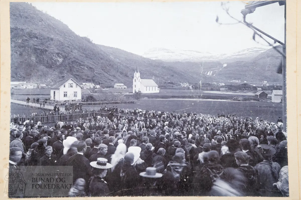 Fotografi. Forsamling, veg, bygninger. Strandebarm kirke i bakgrunnen.
Skrevet bak: 17. mai 1905 eller 1914? Avst. 1905 republikk/konged.?