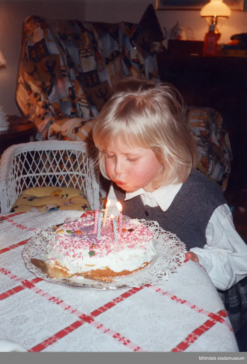 5-årskalas i Lindome, okänt årtal. En okänd liten flicka blåser ut ljus på en tårta. I bakgrunden ses en vit korgstol.