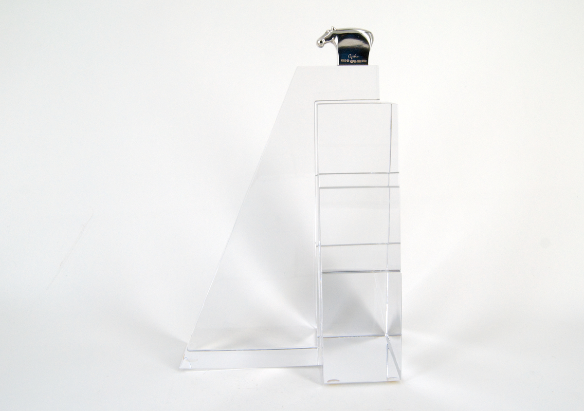 Skulptur, "Litet tempel", i silver och glas, av Gunnar Cyrén, 1989. Högt glasfundament med T-formad bas. Avsmalnande, delvis trappstegsformad, uppåt. Krönt av liten flodhäst i silver.