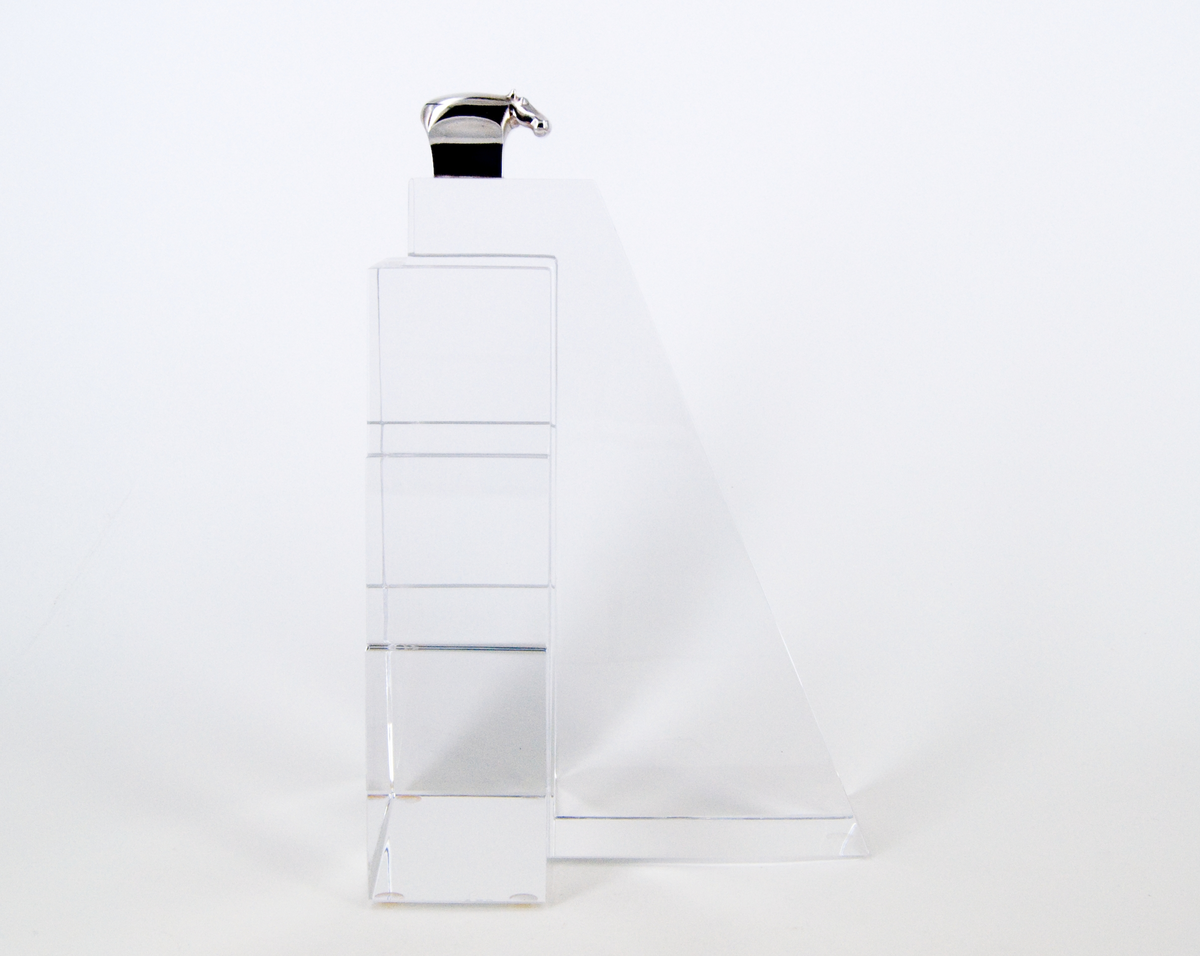Skulptur, "Litet tempel", i silver och glas, av Gunnar Cyrén, 1989. Högt glasfundament med T-formad bas. Avsmalnande, delvis trappstegsformad, uppåt. Krönt av liten flodhäst i silver.
