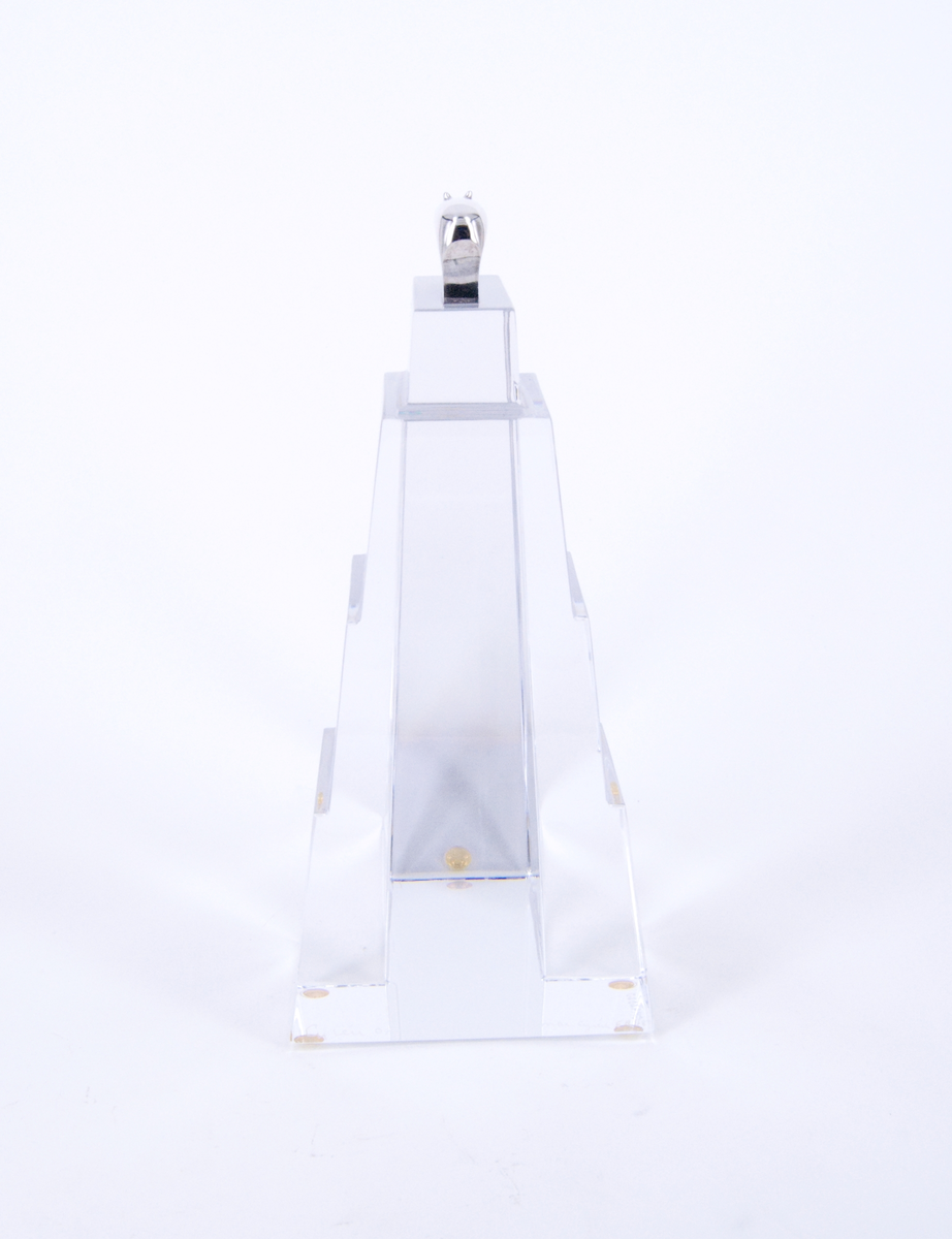 Skulptur, "Litet tempel", i silver och glas, av Gunnar Cyrén, 1989. Högt glasfundament med T-formad bas. Avsmalnande, delvis trappstegsformad, uppåt. Krönt av liten flodhäst i silver.