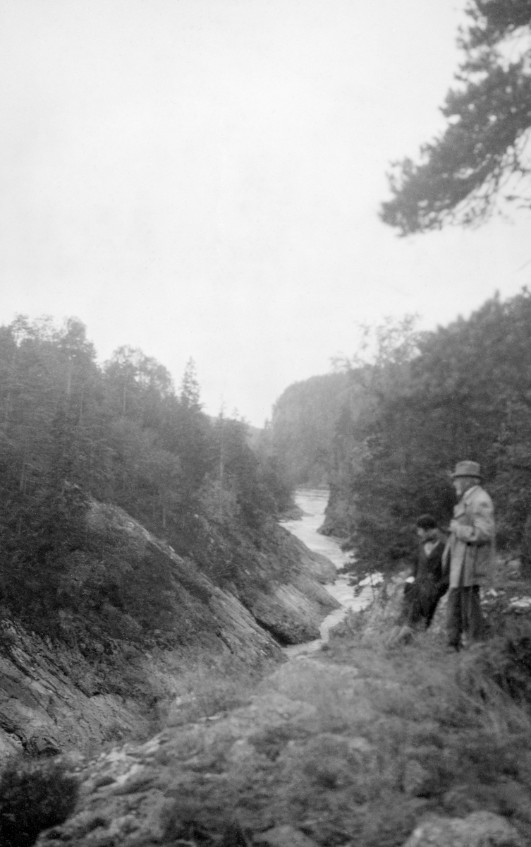 Fra lokaliteten Sølvstua i Ågårdselva i Tune kommune, i det vestre løpet i nedre del av Glommavassdraget.  Fotografiet er tatt fra et berg, der elva gikk i et smalt, djupt gjel med bratte kanter.  Da dette fotografiet ble tatt sto to personer, ei kvinne og en mann, og betraktet utsikten mot det nedenforliggende vassdraget.  Lengre nede ser vi hvordan elva fortsatt flyter mellom forholdsvis steile bergskrenter, men øyensynlig med mindre fall enn ovenfor (til venstre i bildet).