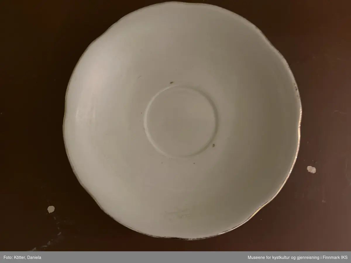Rund porselensfat som brukes under en kopp. Kanten er lett bølget forgyllet.